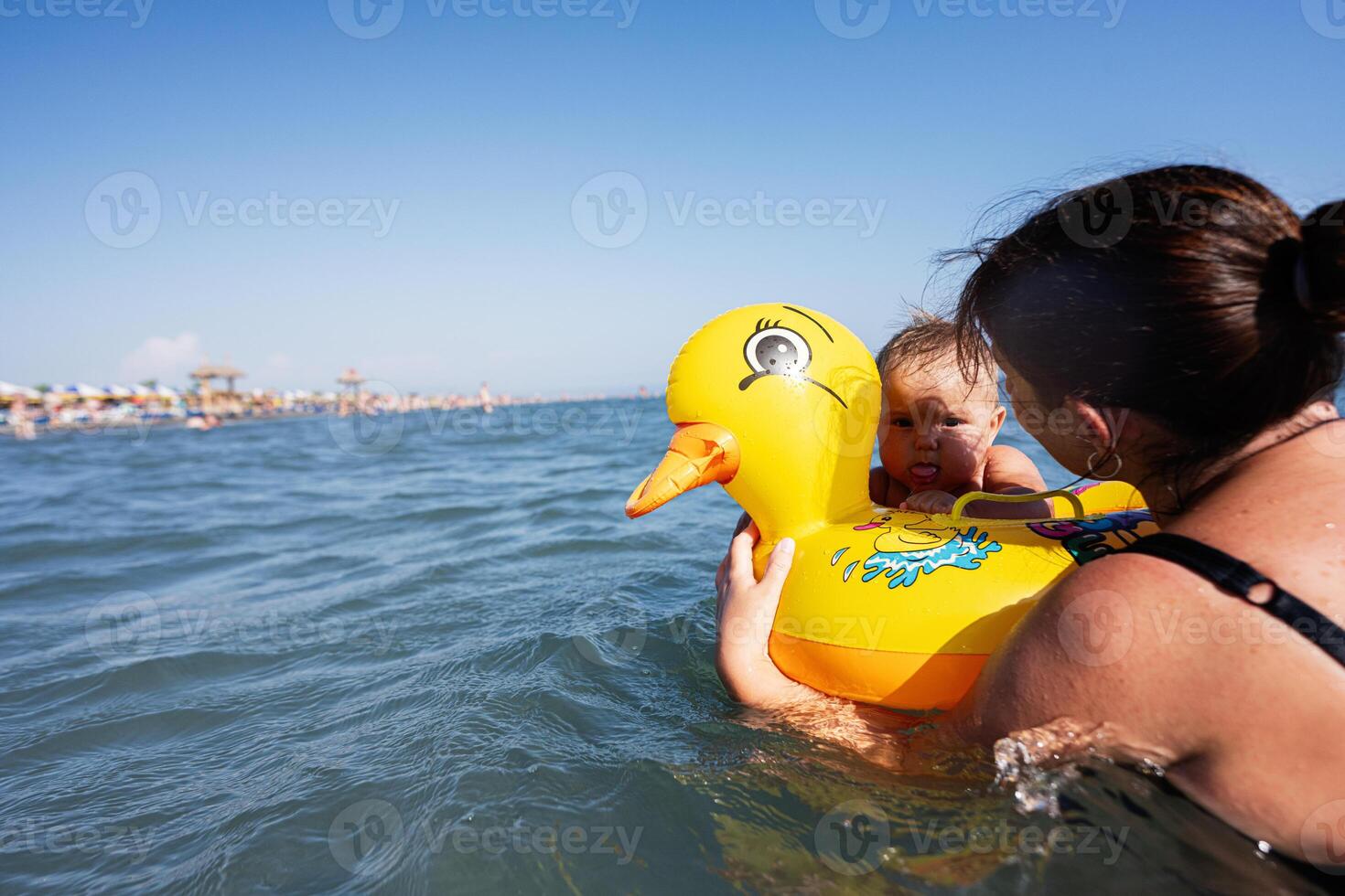 Mother and baby playing in the sea with an inflatable duck float on a sunny day photo