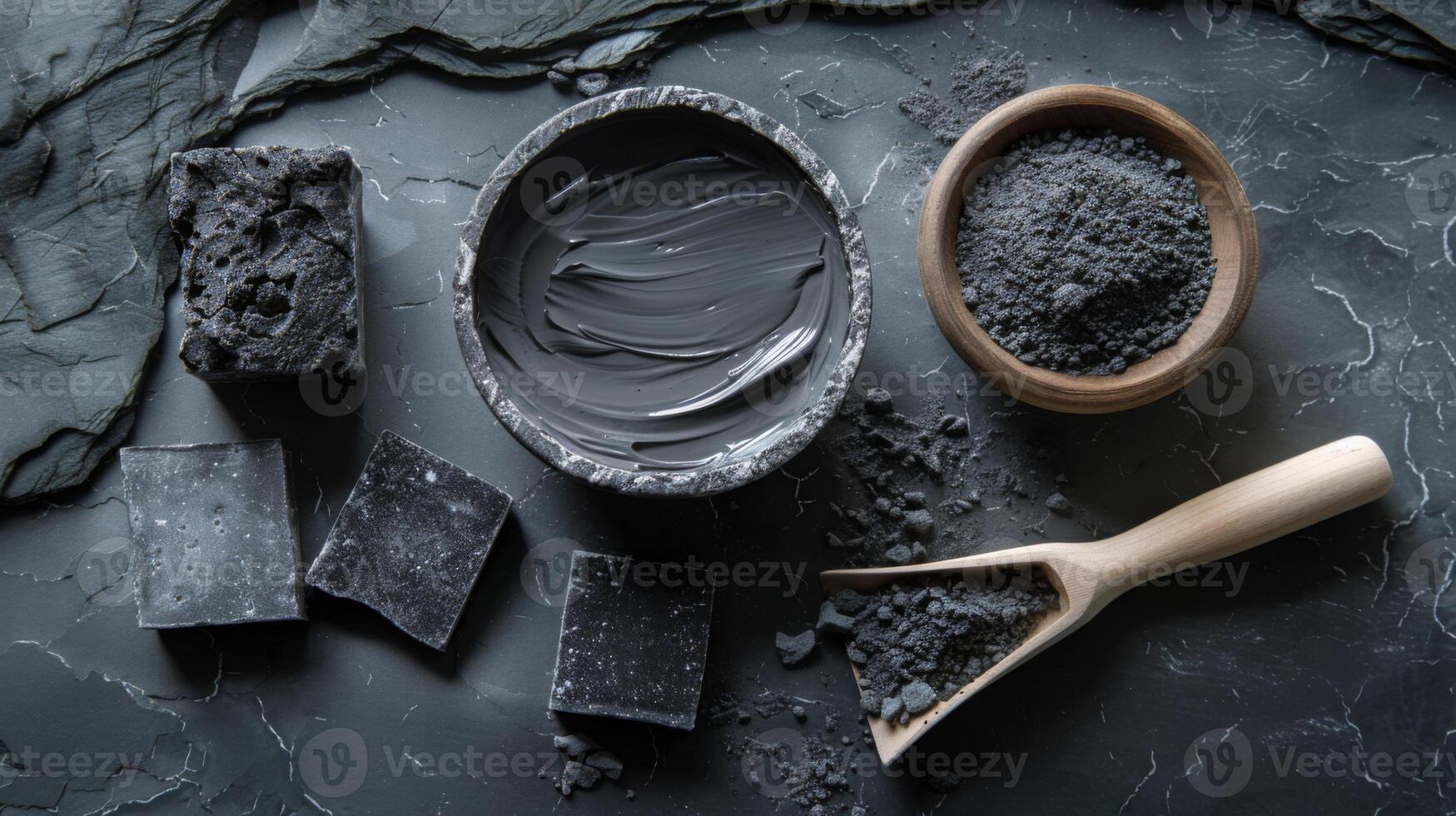 soap bars, a bowl of charcoal powder, a scoop of charcoal powder, and a bowl of charcoal face mask. photo