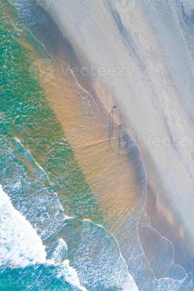top aerial view of three people walking on a beach at sunset, image from a drone. Portugal photo