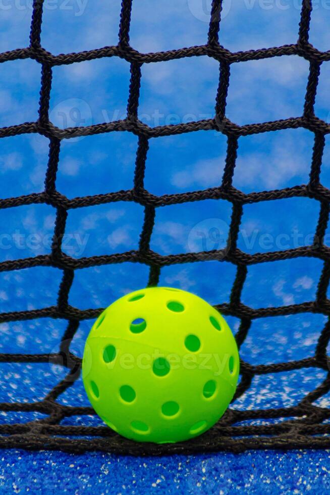 Pickleball ball in front of a blue court net, racket sports photo