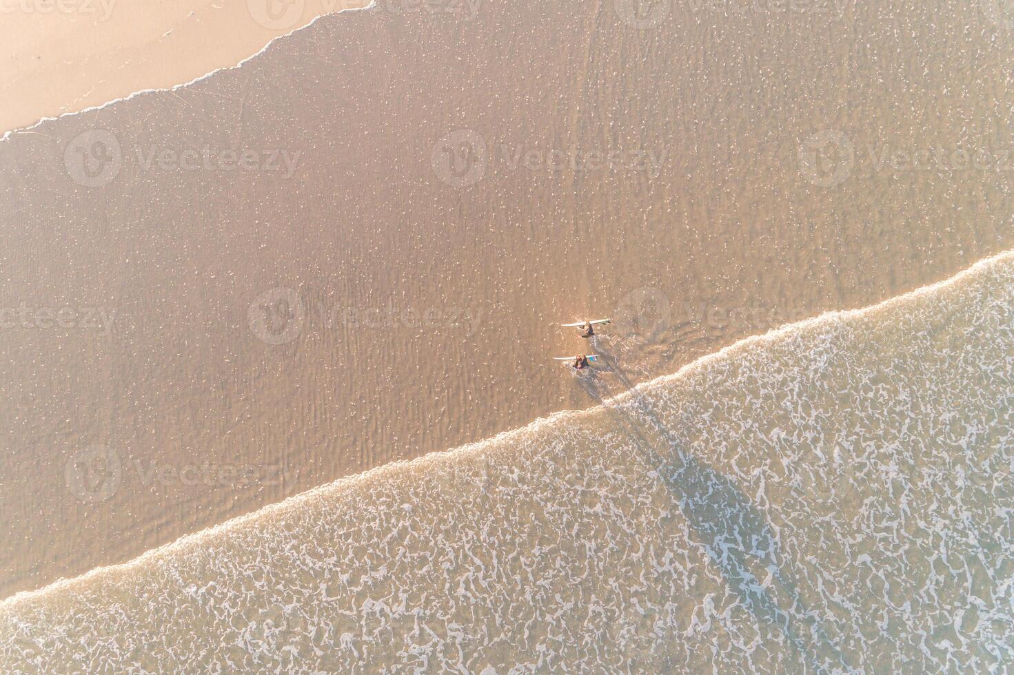 two surfers on the shore of a beach at sunrise, aerial view by drone. Summer concept photo