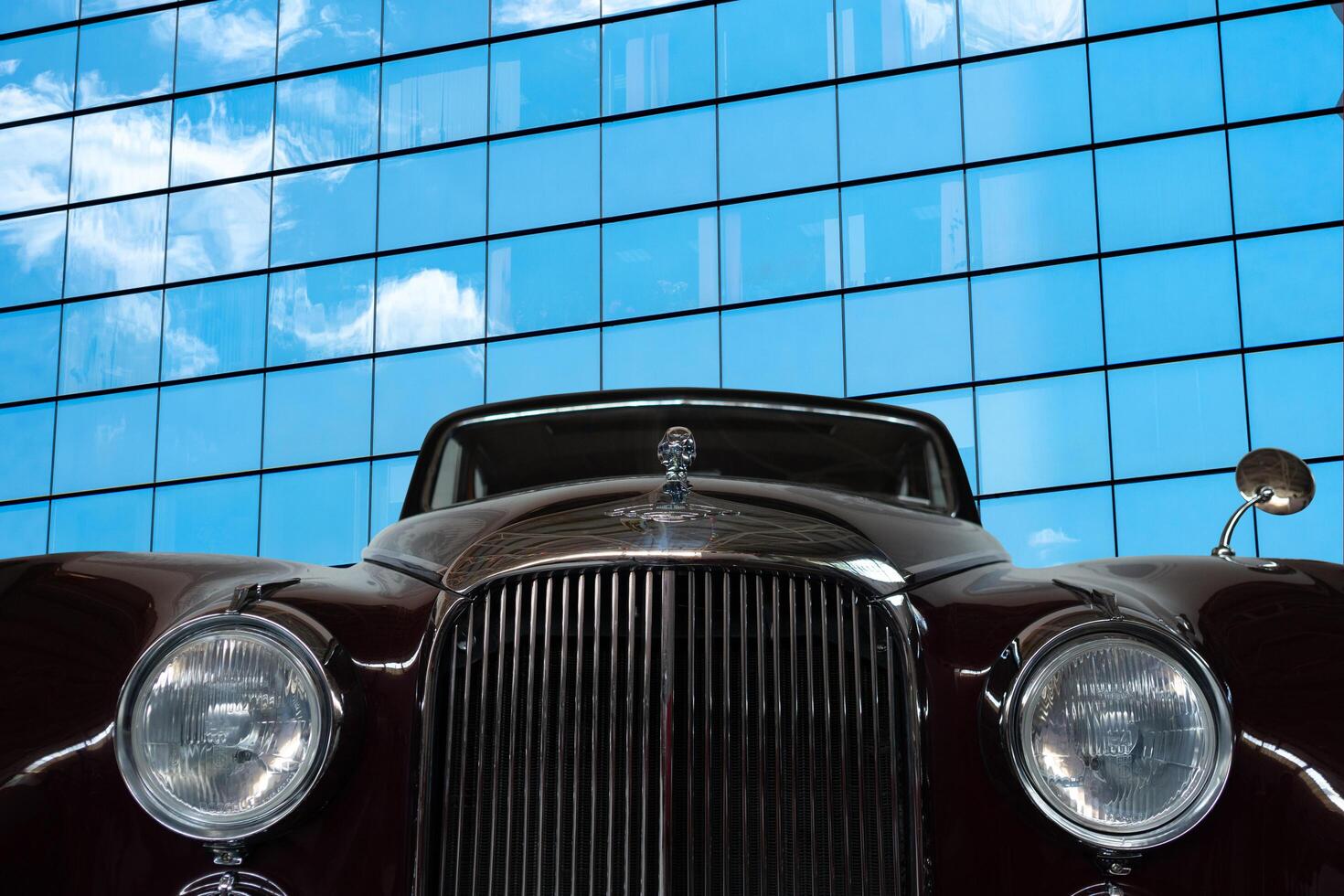 Vintage, black, shiny car on a background of a mirrored wall of a modern building. photo