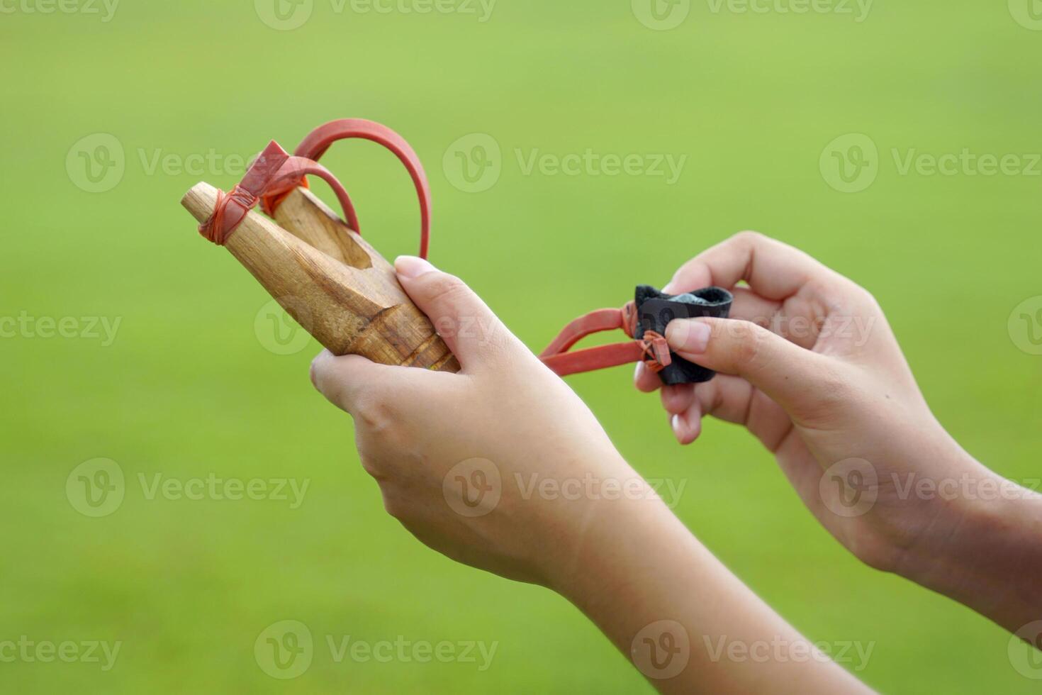 Hand holding Slingshot on green background It is a weapon made from a forked stick with rubber attached to a leather strip that holds bullets to be fired. photo