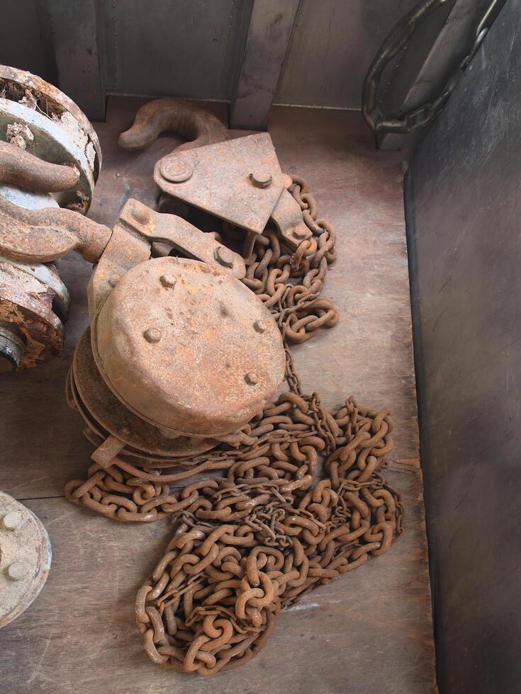 A large, antique, rusted iron pulley with rusted chains lay in a pile below.Photography. photo
