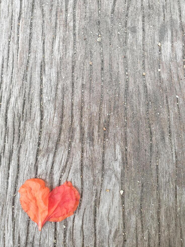 Heart shape from pomegranate petals on gray old wood, clear cracks in the wood, grains of sand on the cracks photo