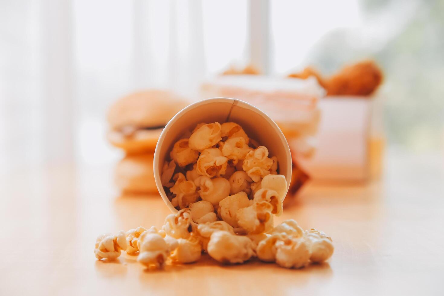 A bucket of popcorn, top-view, warm colors, light brown wooden background, flat lay, daylight macro close-up photo