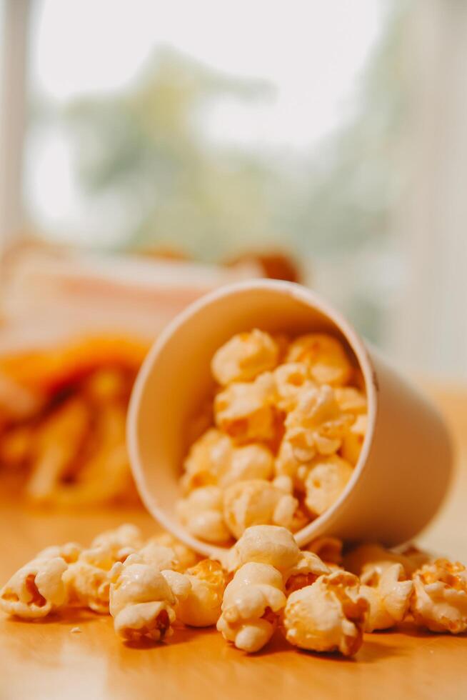 A bucket of popcorn, top-view, warm colors, light brown wooden background, flat lay, daylight macro close-up photo