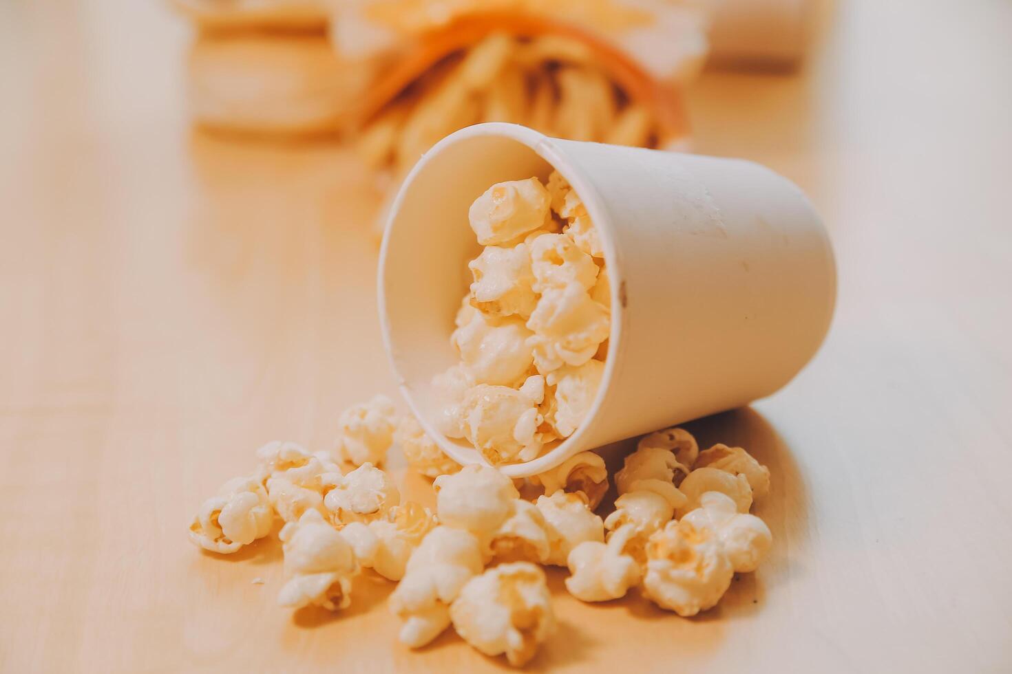 A bucket of popcorn, top-view, warm colors, light brown wooden background, flat lay, daylight macro close-up photo