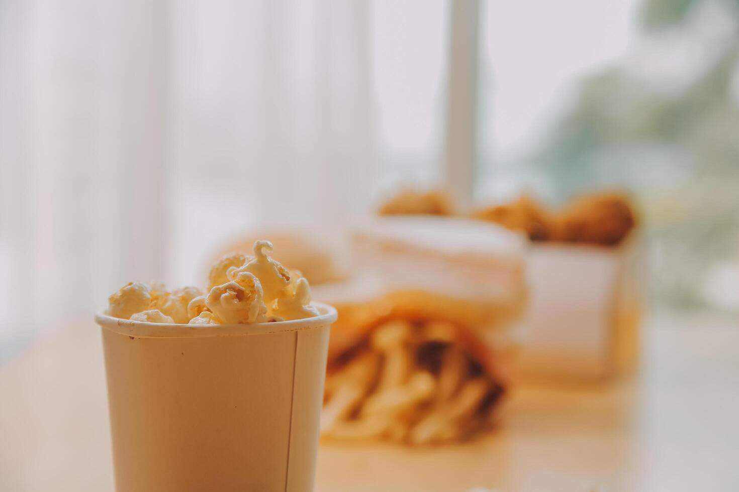A bucket of popcorn, top-view, warm colors, light brown wooden background, flat lay, daylight macro close-up photo