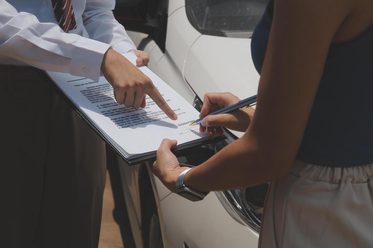 Side view of writing on clipboard while insurance agent examining car after accident photo