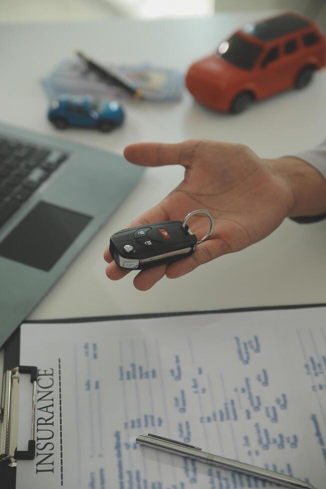 Young man receives a key from car salesman. After agreeing to a contract for rent or sale of a car at workshop, loan car, insurance, sale, buying car and finance concept. photo