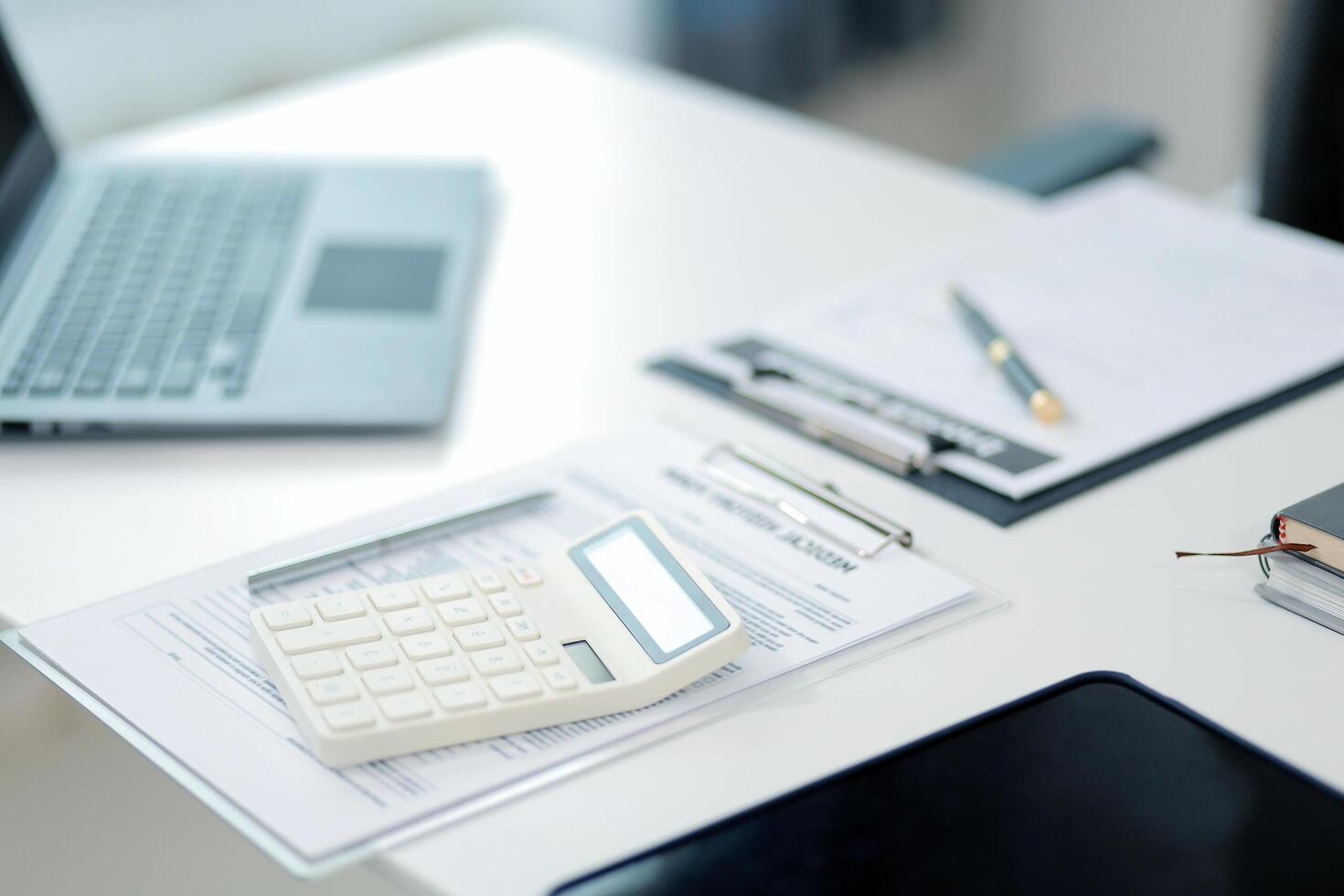 Doctor's working on laptop computer, writing prescription clipboard with record information paper folders on desk in hospital or clinic, Healthcare and medical concept. Focus on stethoscope photo