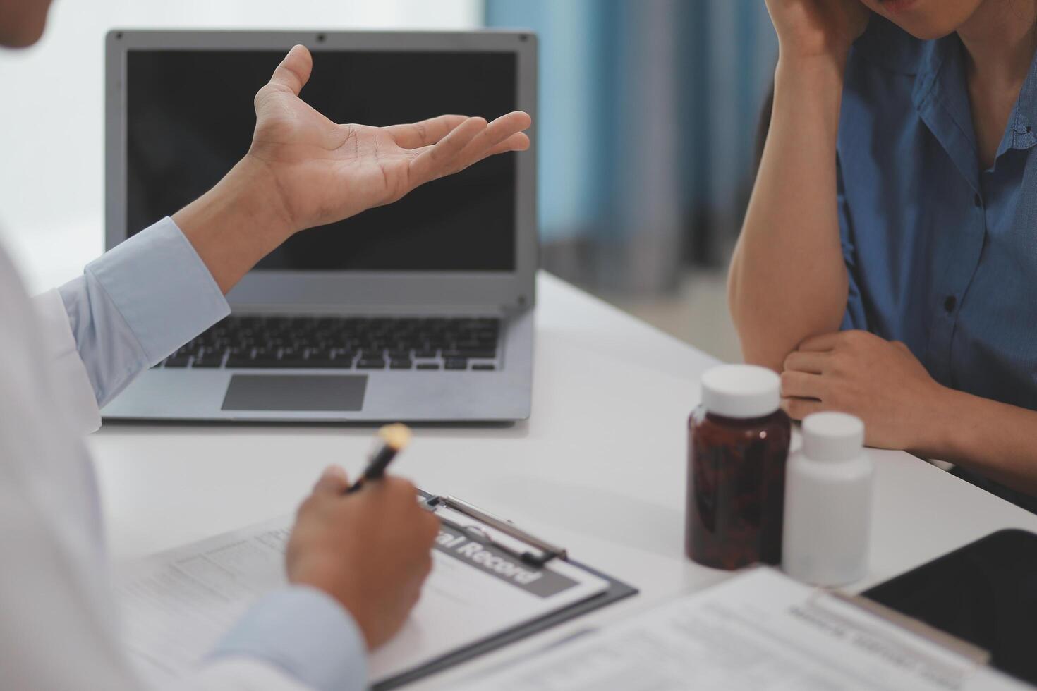 Doctor and patient sitting near each other at the wooden desk in clinic. Female physician's pointing to a records form. Medicine concept photo