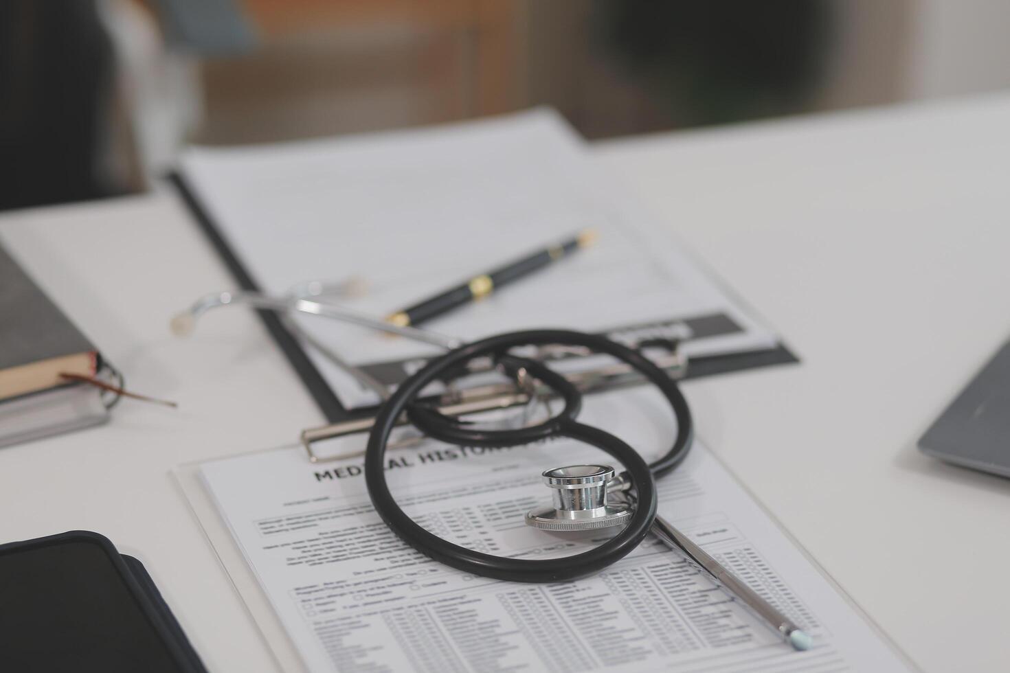 Doctor's working on laptop computer, writing prescription clipboard with record information paper folders on desk in hospital or clinic, Healthcare and medical concept. Focus on stethoscope photo