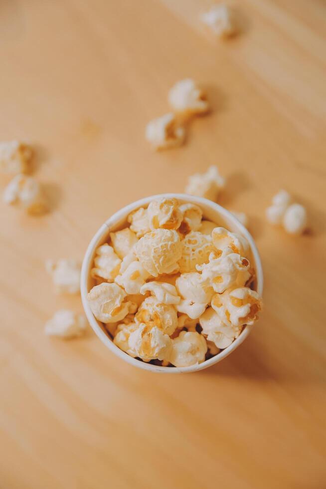 A bucket of popcorn, top-view, warm colors, light brown wooden background, flat lay, daylight macro close-up photo