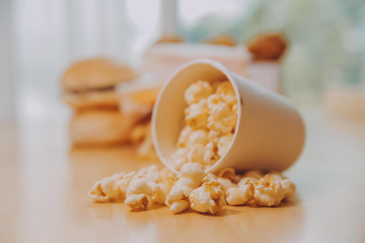 A bucket of popcorn, top-view, warm colors, light brown wooden background, flat lay, daylight macro close-up photo