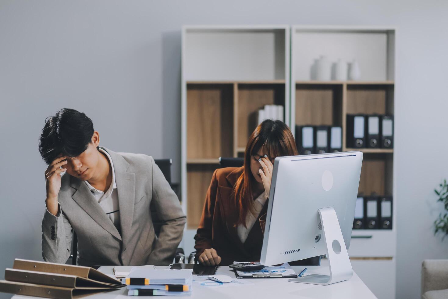 Stressed business couple working at big cabinet. Frustrated director closed face with hands at laptop workplace interior. Woman partner solving problems on smartphone call feeling nervous at office photo