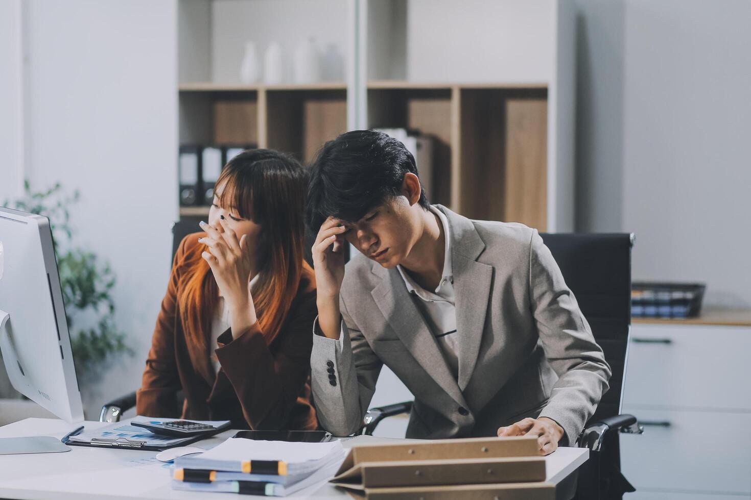 Stressed business couple working at big cabinet. Frustrated director closed face with hands at laptop workplace interior. Woman partner solving problems on smartphone call feeling nervous at office photo
