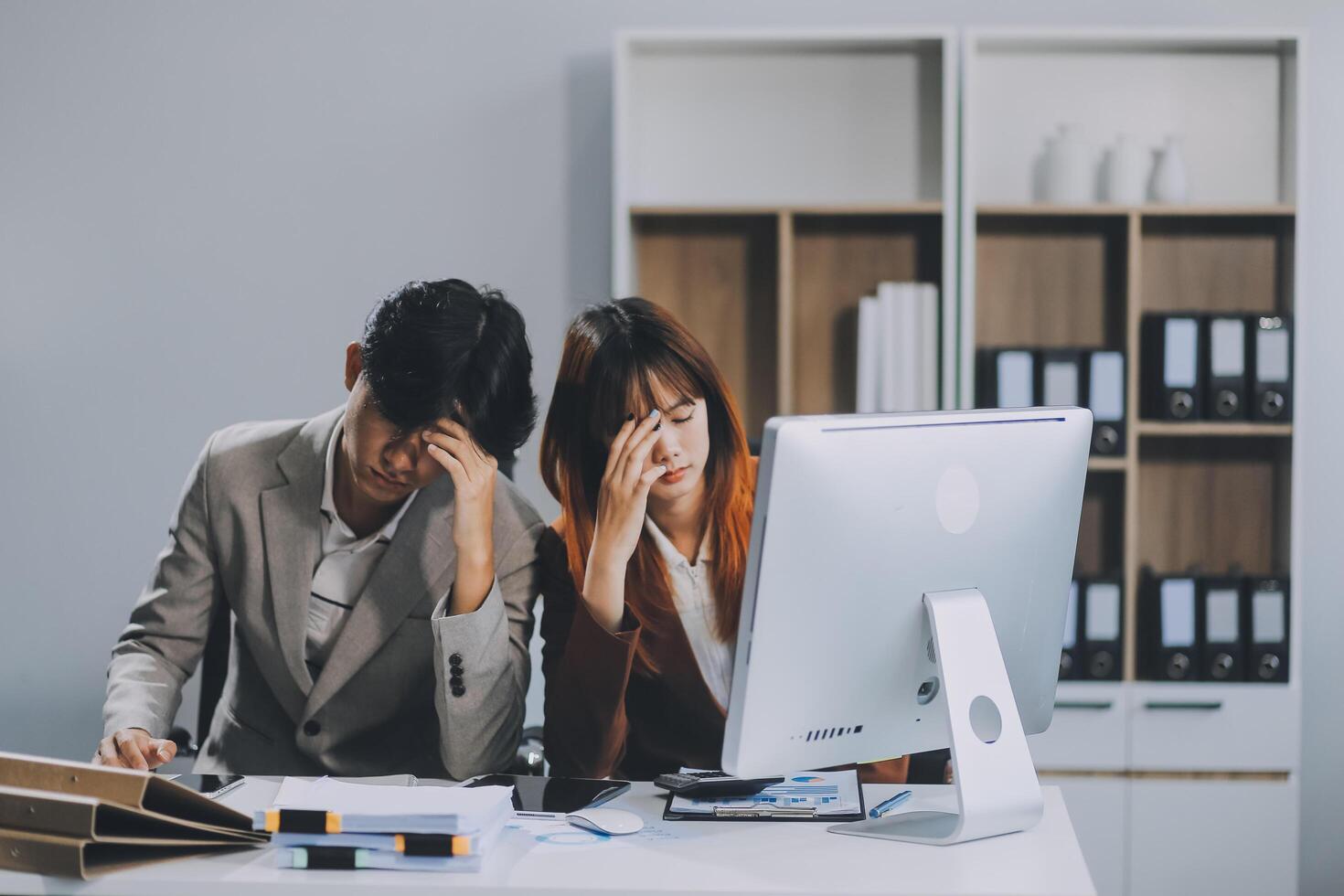 Stressed business couple working at big cabinet. Frustrated director closed face with hands at laptop workplace interior. Woman partner solving problems on smartphone call feeling nervous at office photo