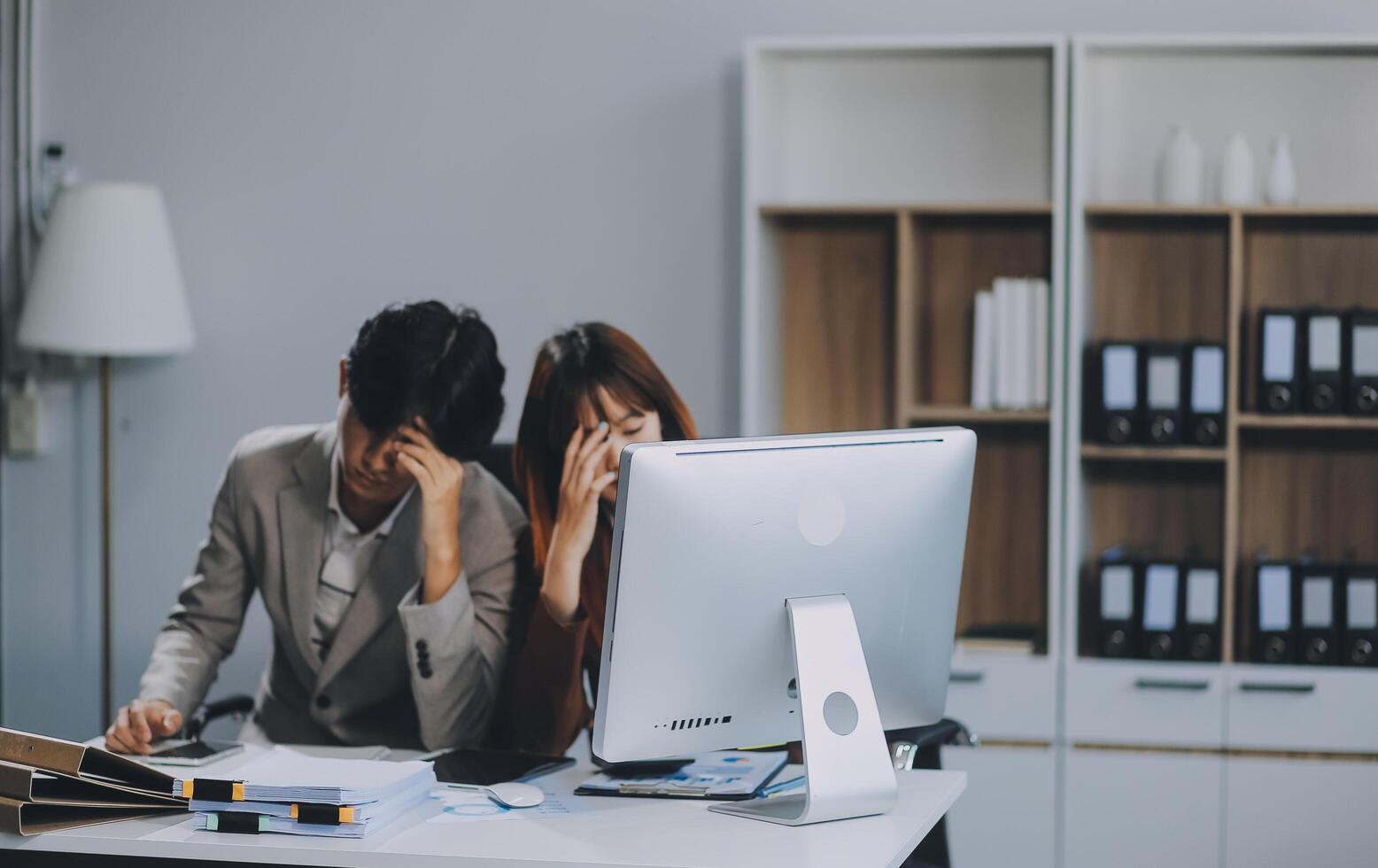 Stressed business couple working at big cabinet. Frustrated director closed face with hands at laptop workplace interior. Woman partner solving problems on smartphone call feeling nervous at office photo