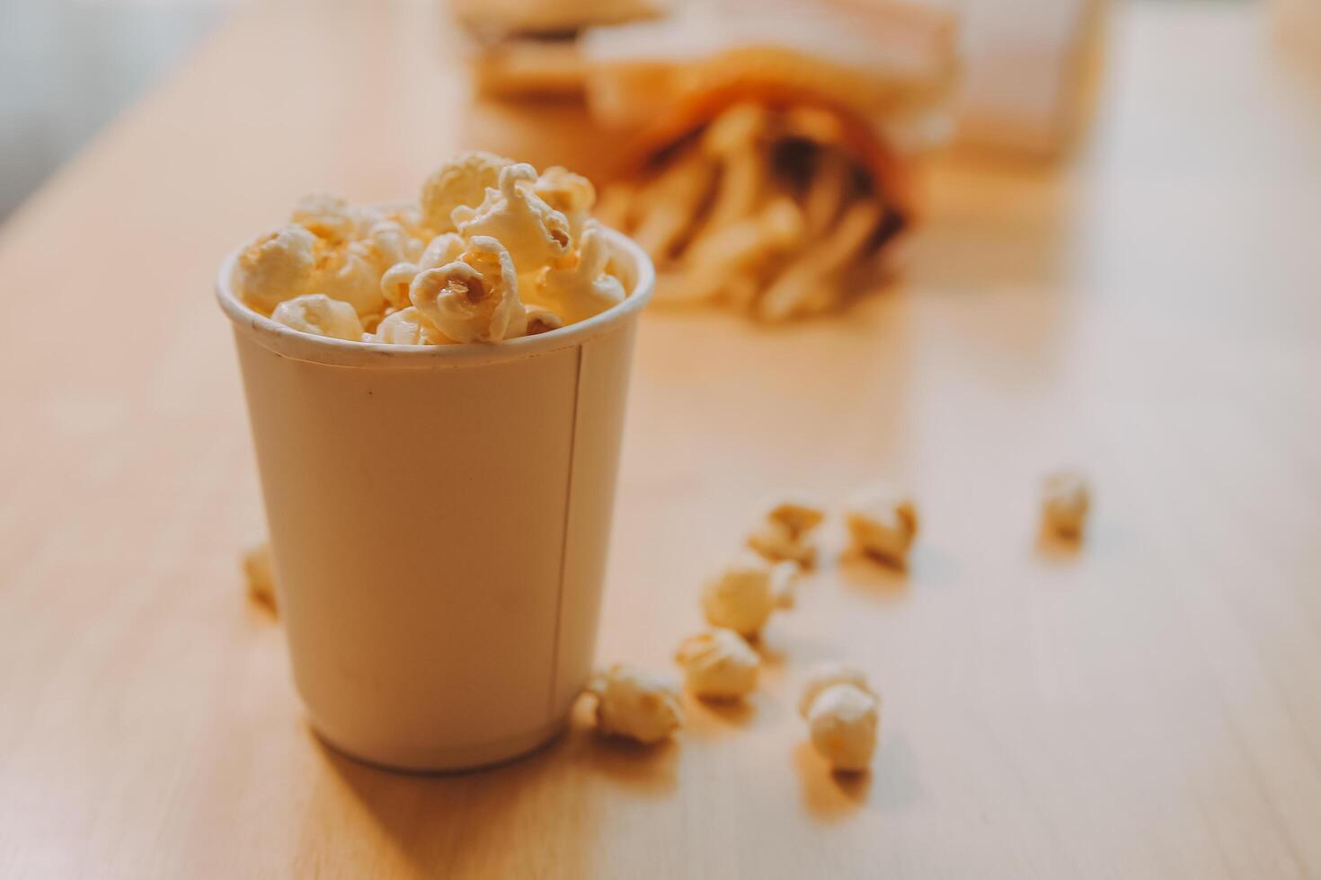 A bucket of popcorn, top-view, warm colors, light brown wooden background, flat lay, daylight macro close-up photo