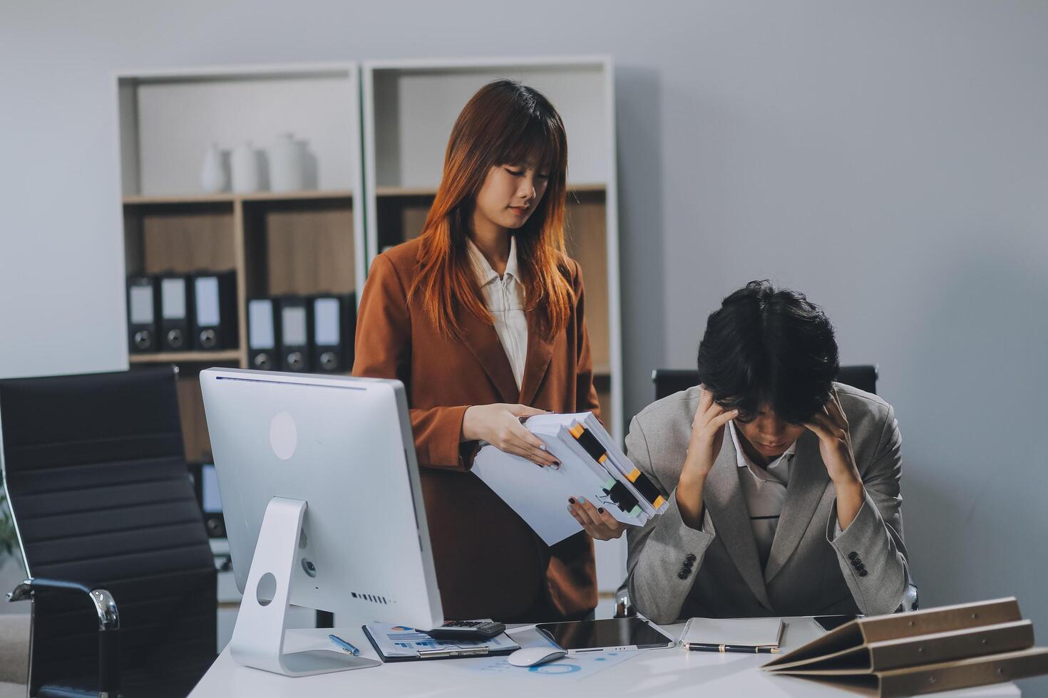Stressed business couple working at big cabinet. Frustrated director closed face with hands at laptop workplace interior. Woman partner solving problems on smartphone call feeling nervous at office photo
