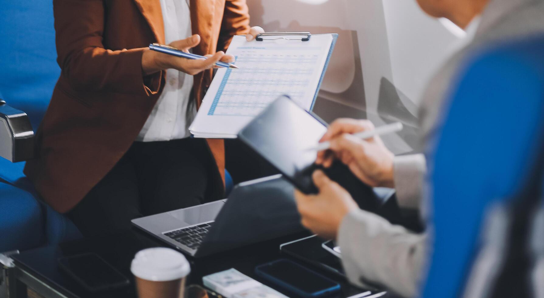business people at meeting in private plane, Asian businessman in suit is talking to woman in jet and pointing at blank laptop screen, colleagues are discussing deal and flying in plane photo