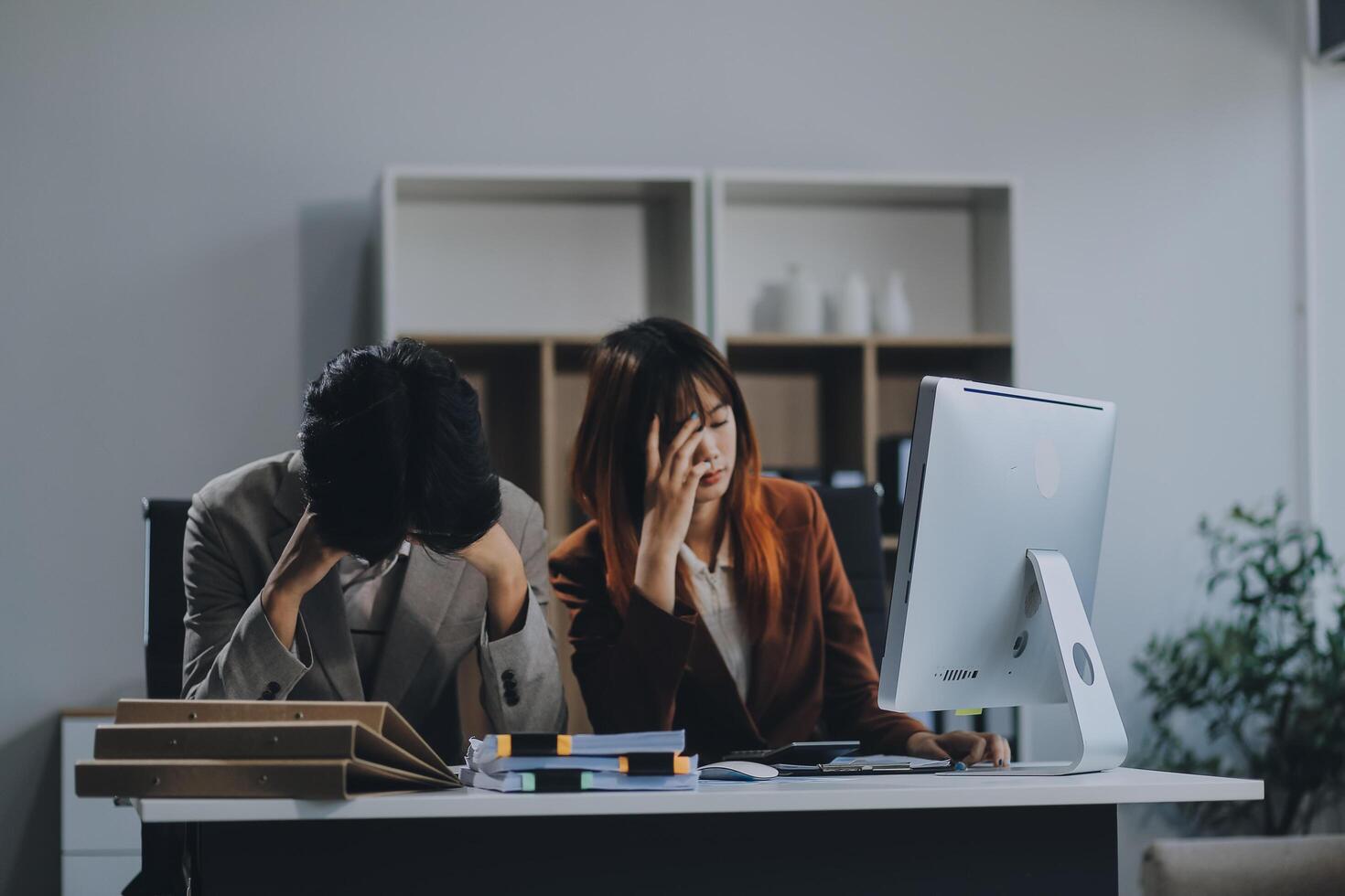 Stressed business couple working at big cabinet. Frustrated director closed face with hands at laptop workplace interior. Woman partner solving problems on smartphone call feeling nervous at office photo