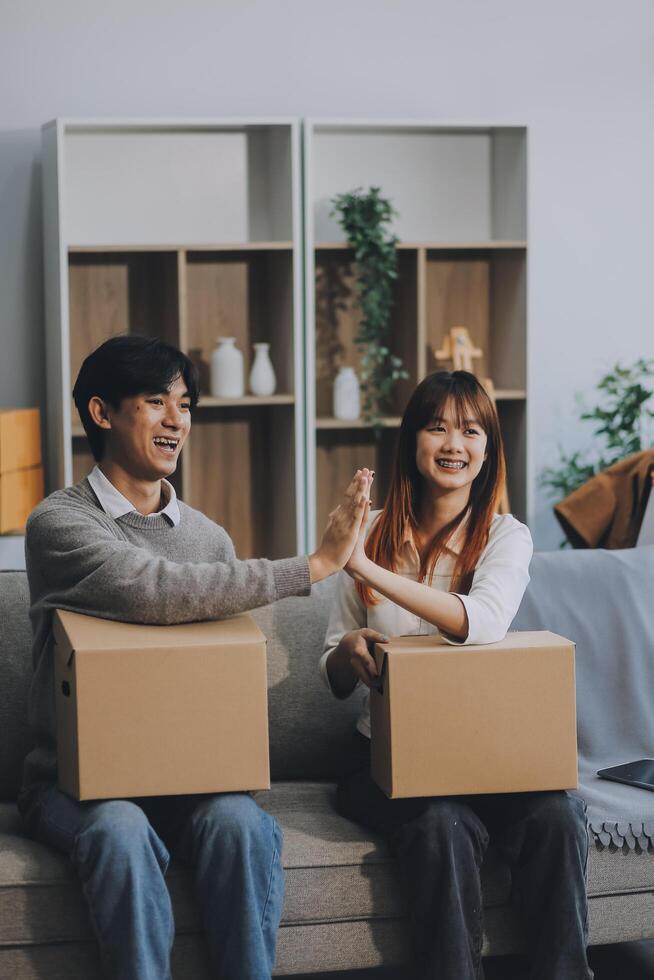 Young Asian couple relocating to a new house, joyfully packing and unpacking belongings. Expertise in moving, packing, togetherness, and creating a new home together. photo
