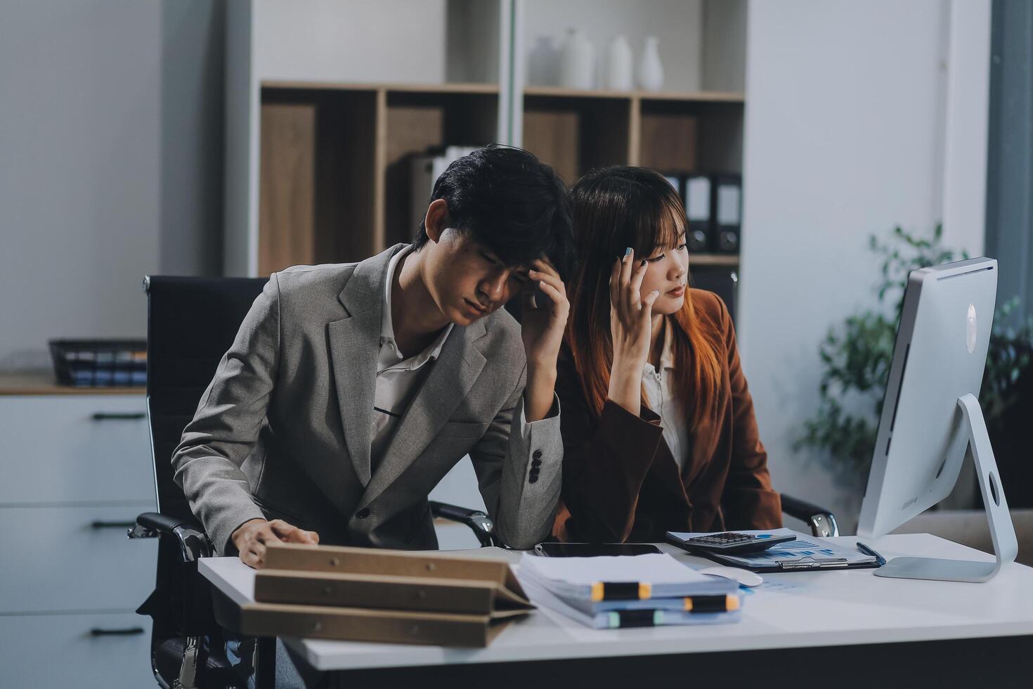 Stressed business couple working at big cabinet. Frustrated director closed face with hands at laptop workplace interior. Woman partner solving problems on smartphone call feeling nervous at office photo