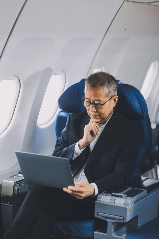Attractive Asian male passenger of airplane sitting in comfortable seat while working laptop and tablet with mock up area using wireless connection. Travel in style, work with grace. photo
