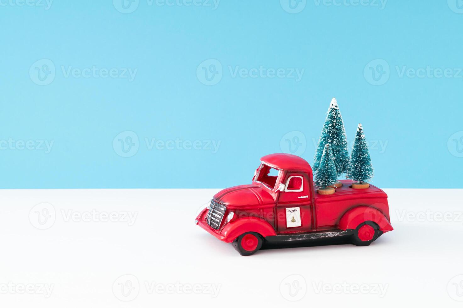 Creative layout made with red Christmas retro truck and green Christmas trees on white and light blue background. Minimal Christmas and New Year concept. Festive holiday composition. Xmas aesthetic. photo