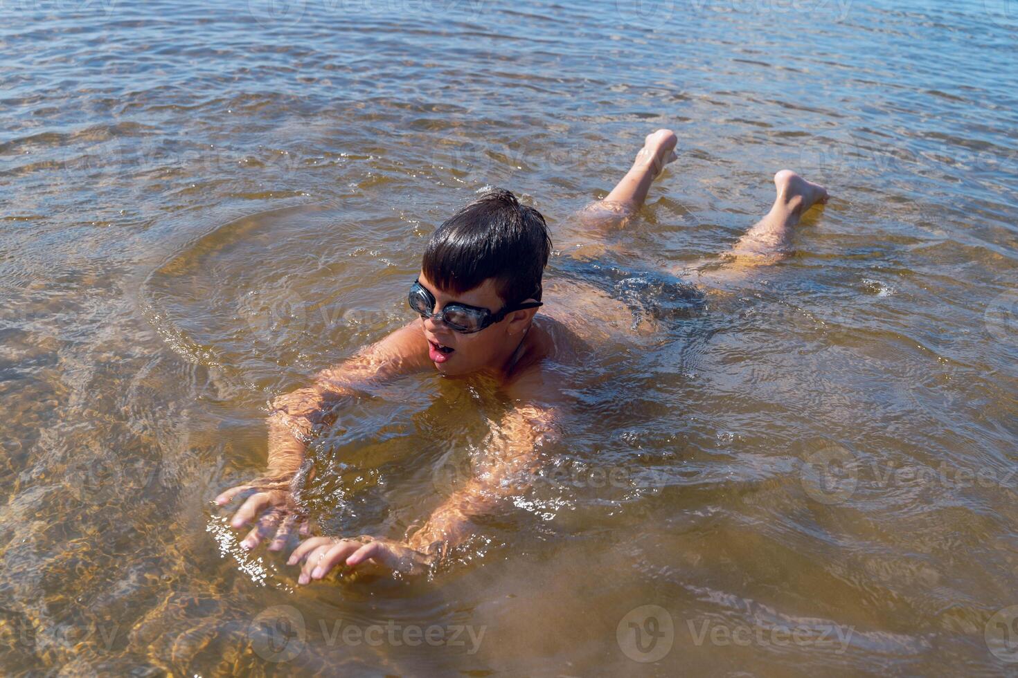 A boy swims energetically in a serene lake while wearing goggles photo