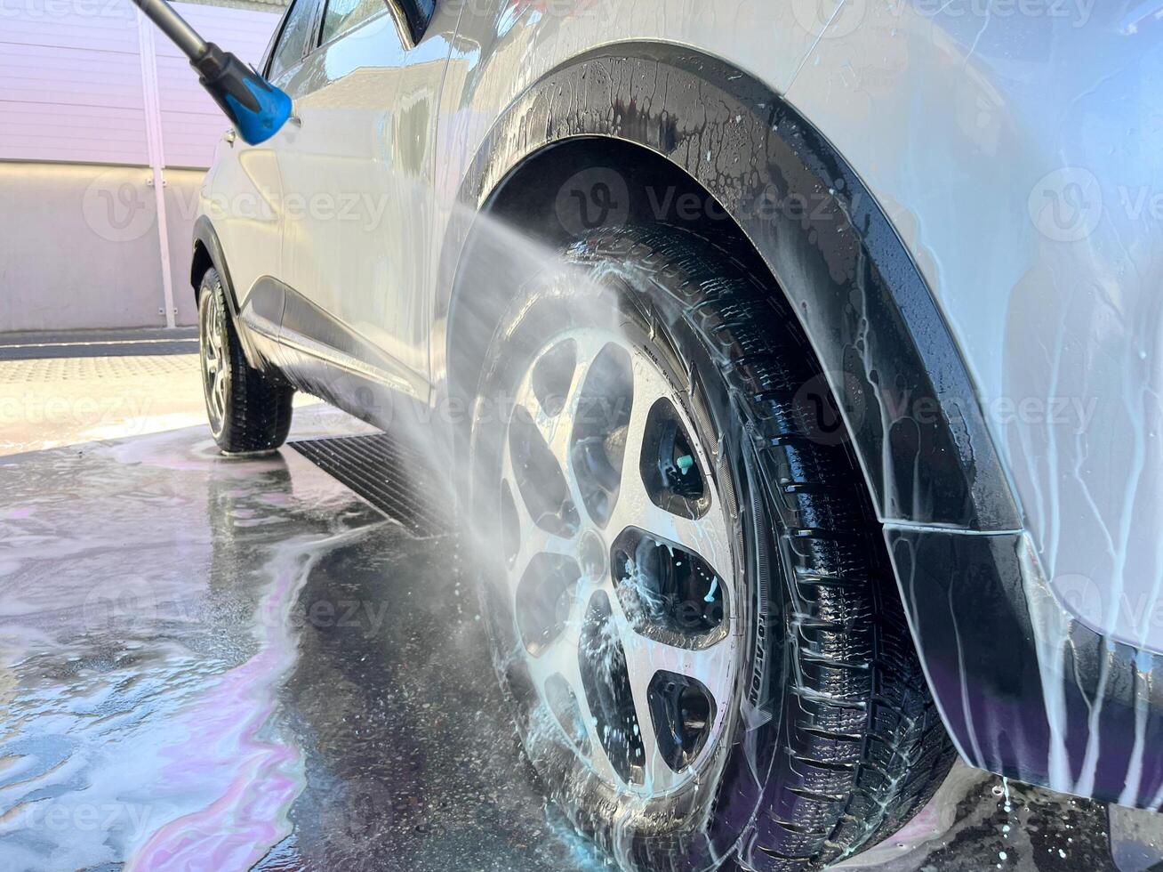 A silver car at a car wash after cleaning with active foam, wax is applied photo