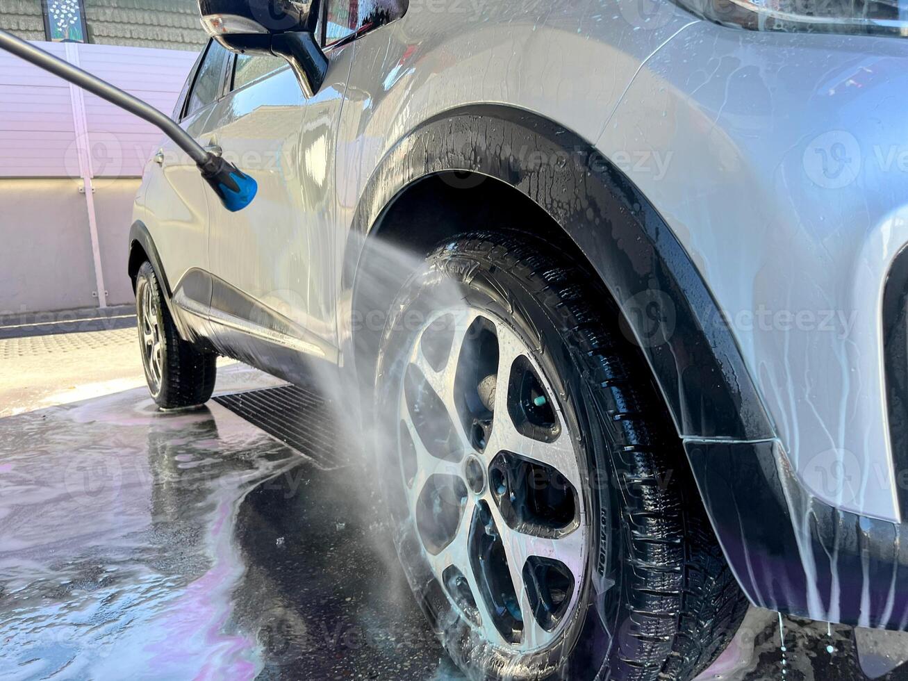 A silver car at a car wash after cleaning with active foam, wax is applied photo