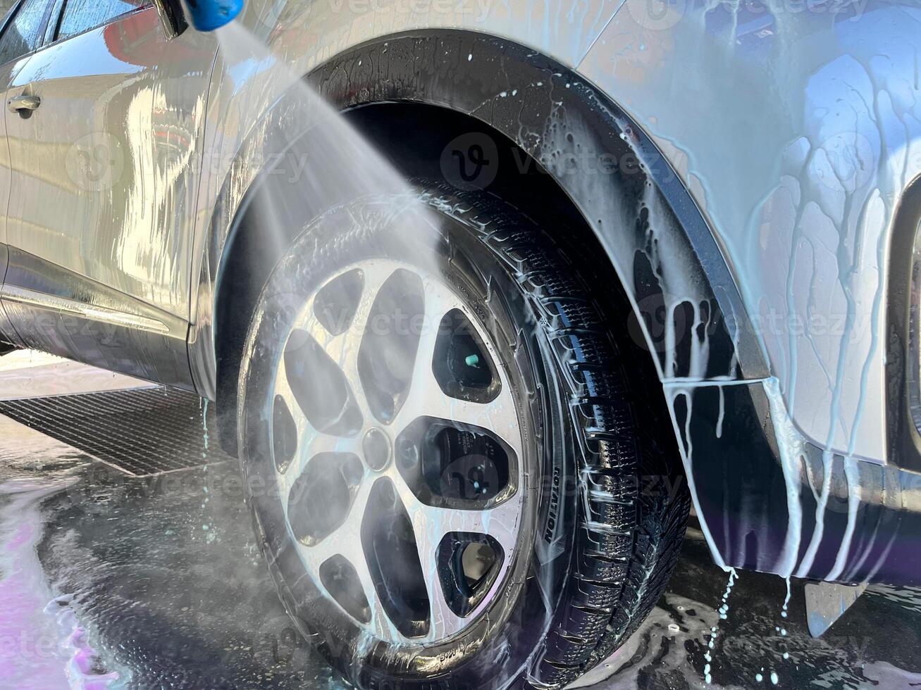 A silver car at a car wash after cleaning with active foam, wax is applied photo