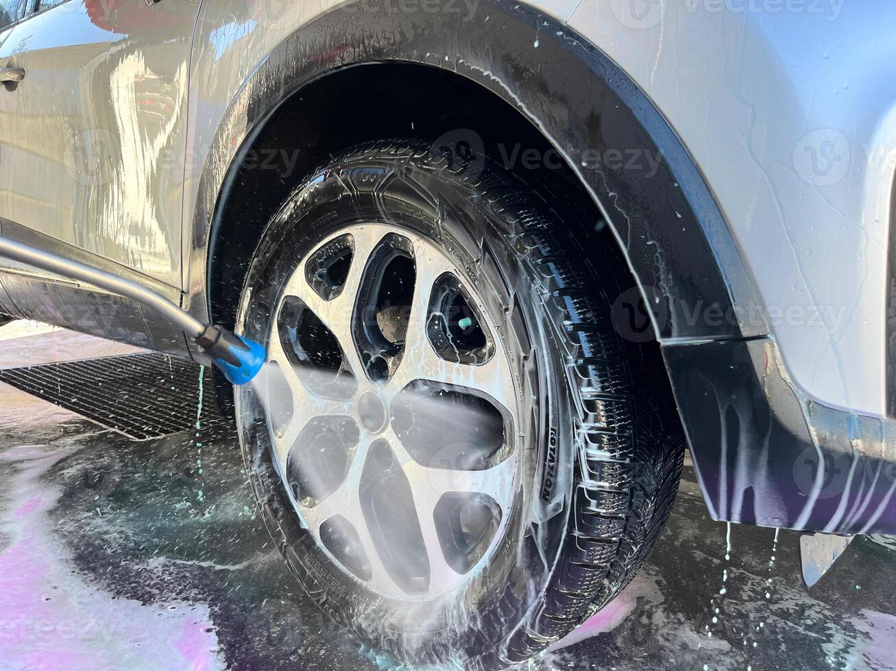 A silver car at a car wash after cleaning with active foam, wax is applied photo