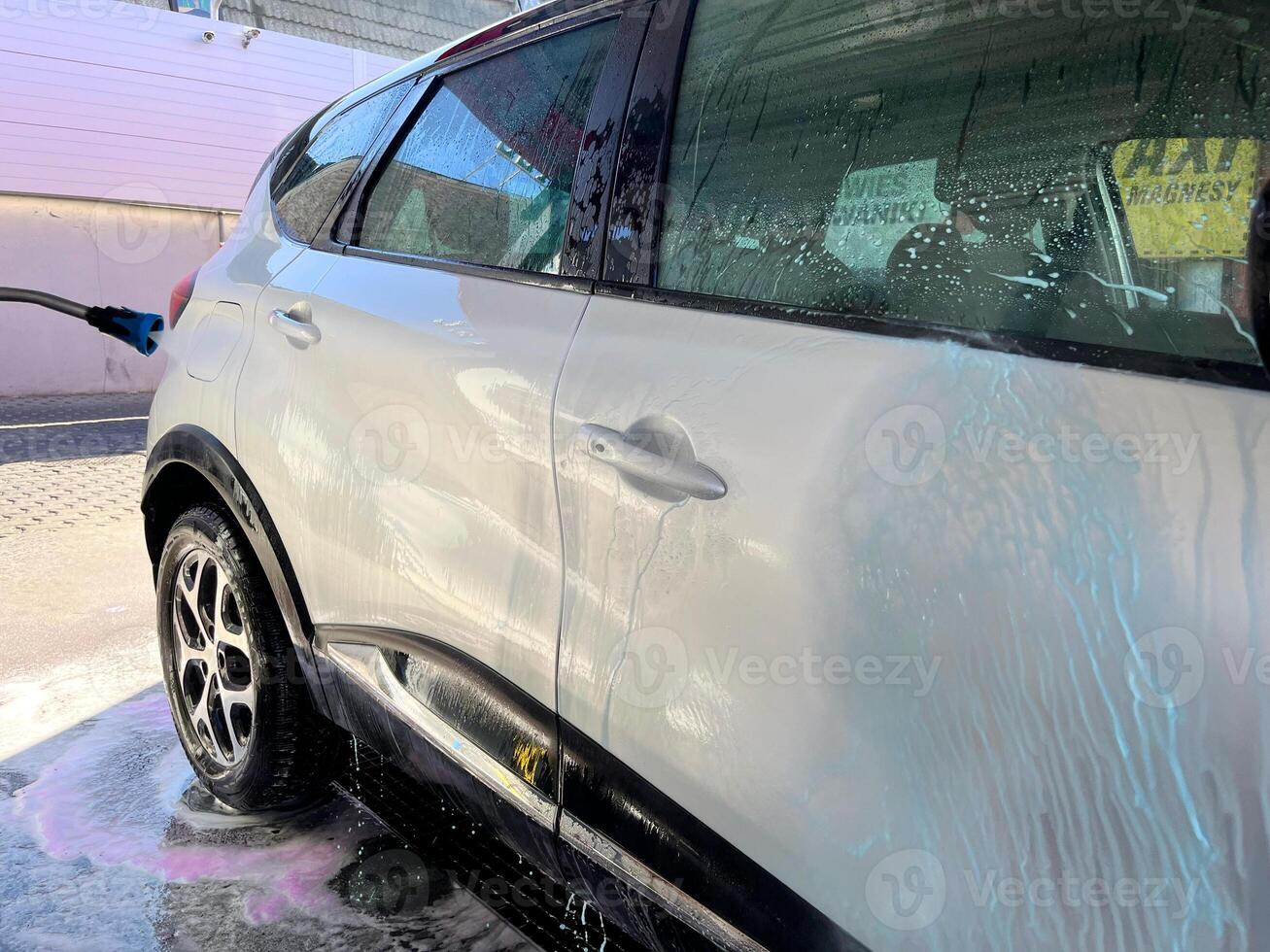 A silver car at a car wash after cleaning with active foam, wax is applied photo