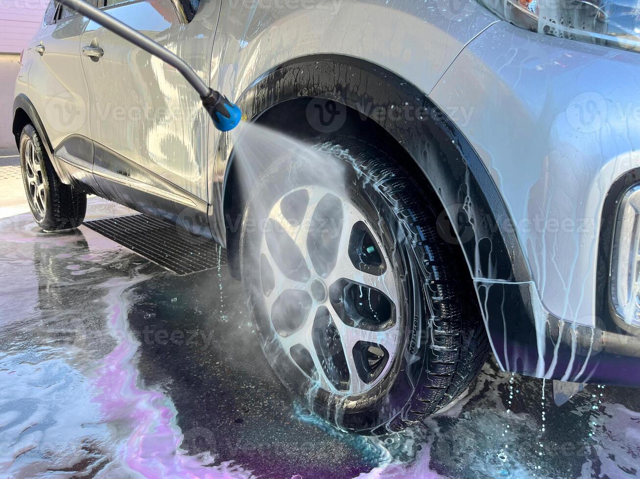 A silver car at a car wash after cleaning with active foam, wax is applied photo