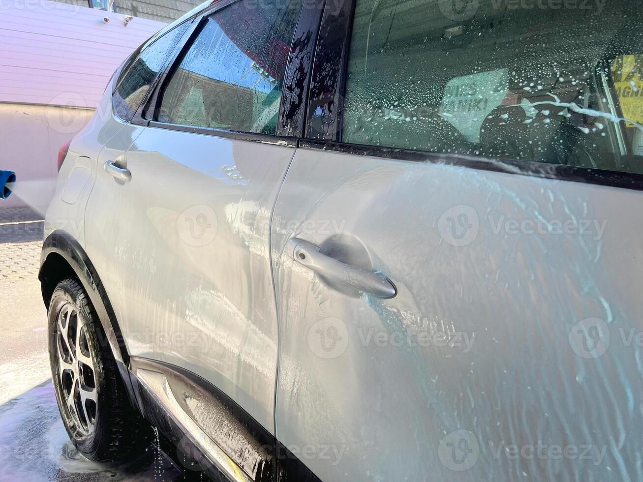 A silver car at a car wash after cleaning with active foam, wax is applied photo
