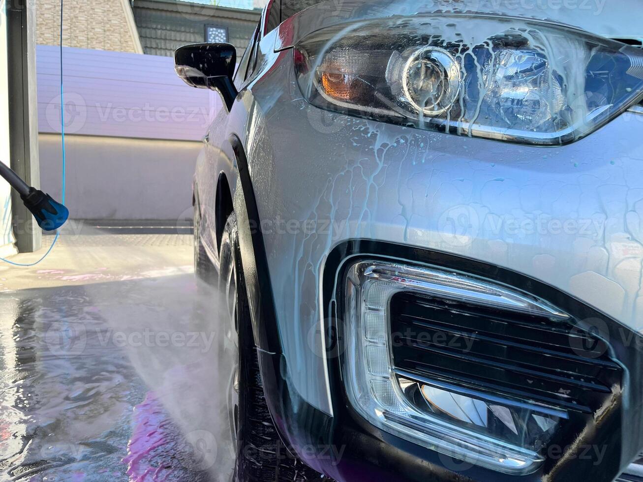 A silver car at a car wash after cleaning with active foam, wax is applied photo