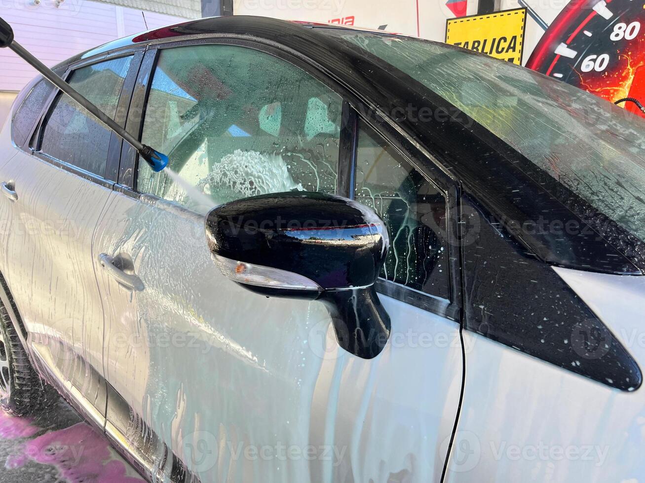 A silver car at a car wash after cleaning with active foam, wax is applied photo