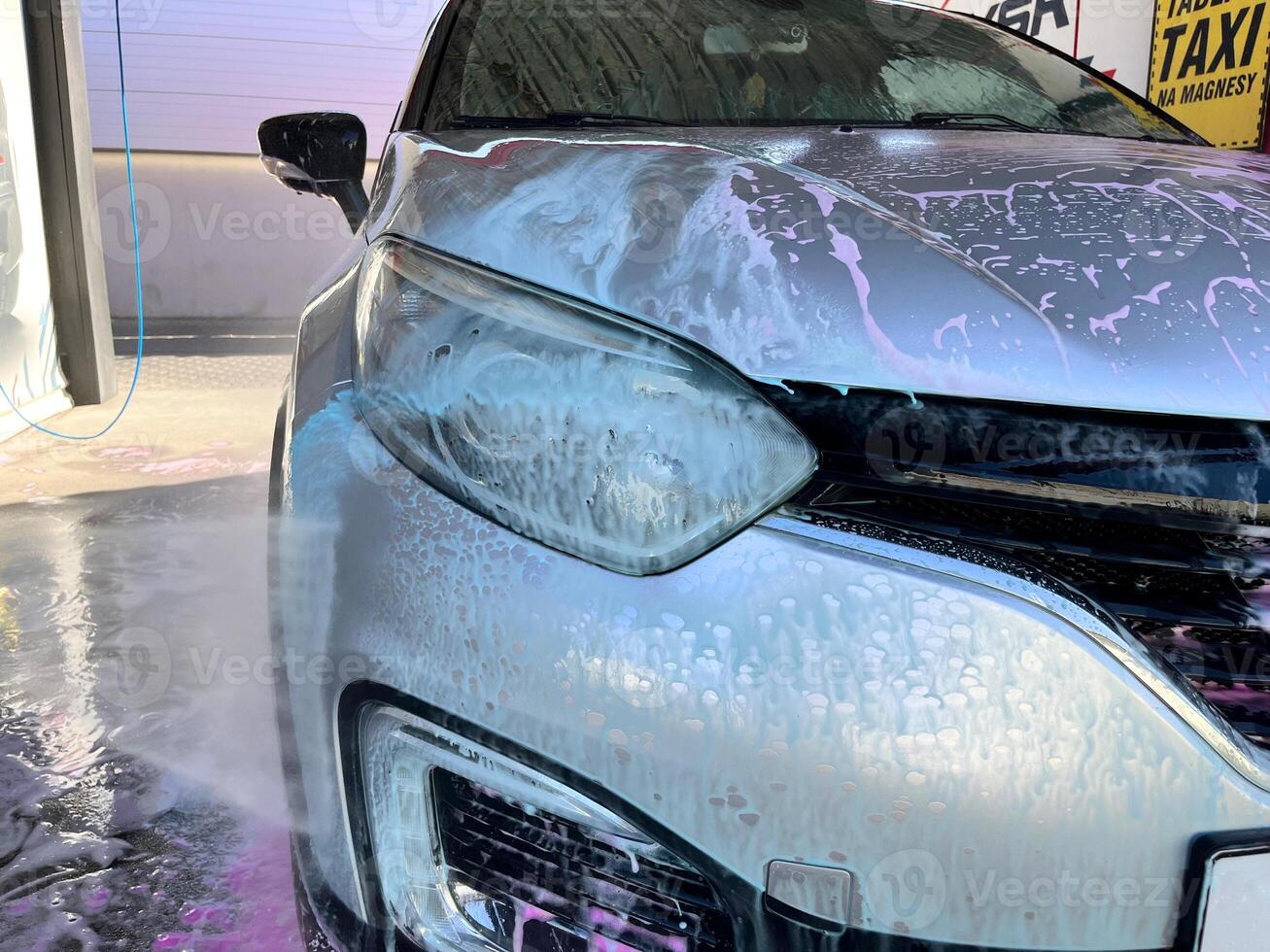 A silver car at a car wash after cleaning with active foam, wax is applied photo