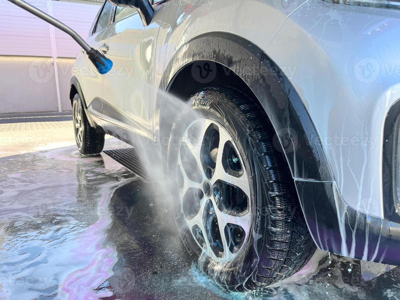 A silver car at a car wash after cleaning with active foam, wax is applied photo
