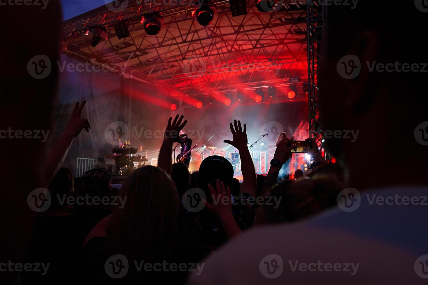 Silhouettes of crowd at concert in front of stage with bright spotlights. People enjoy live music at the band's performance. Concert hall with musicians on stage and fans during music festival photo