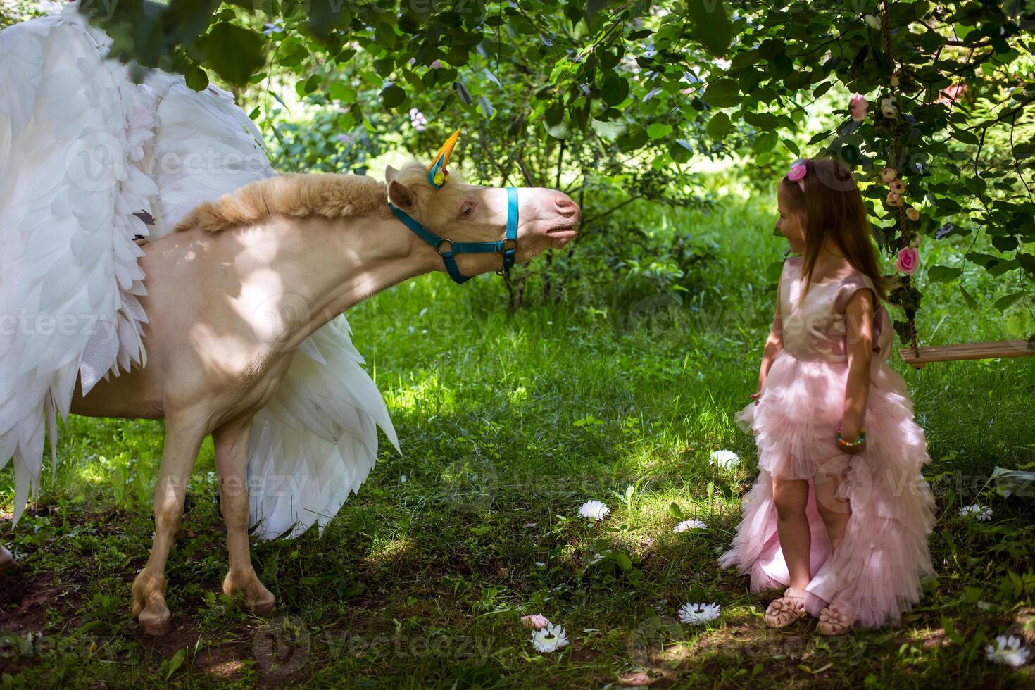 Cheerful cute girl playing and hugging magical unicorn. photo