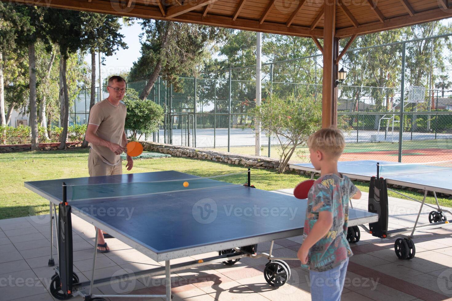 eight year old blond boy plays ping pong with his father on a special table tennis court, fun summer sports activities for children, unforgettable summer holidays with the whole family in Turkey photo