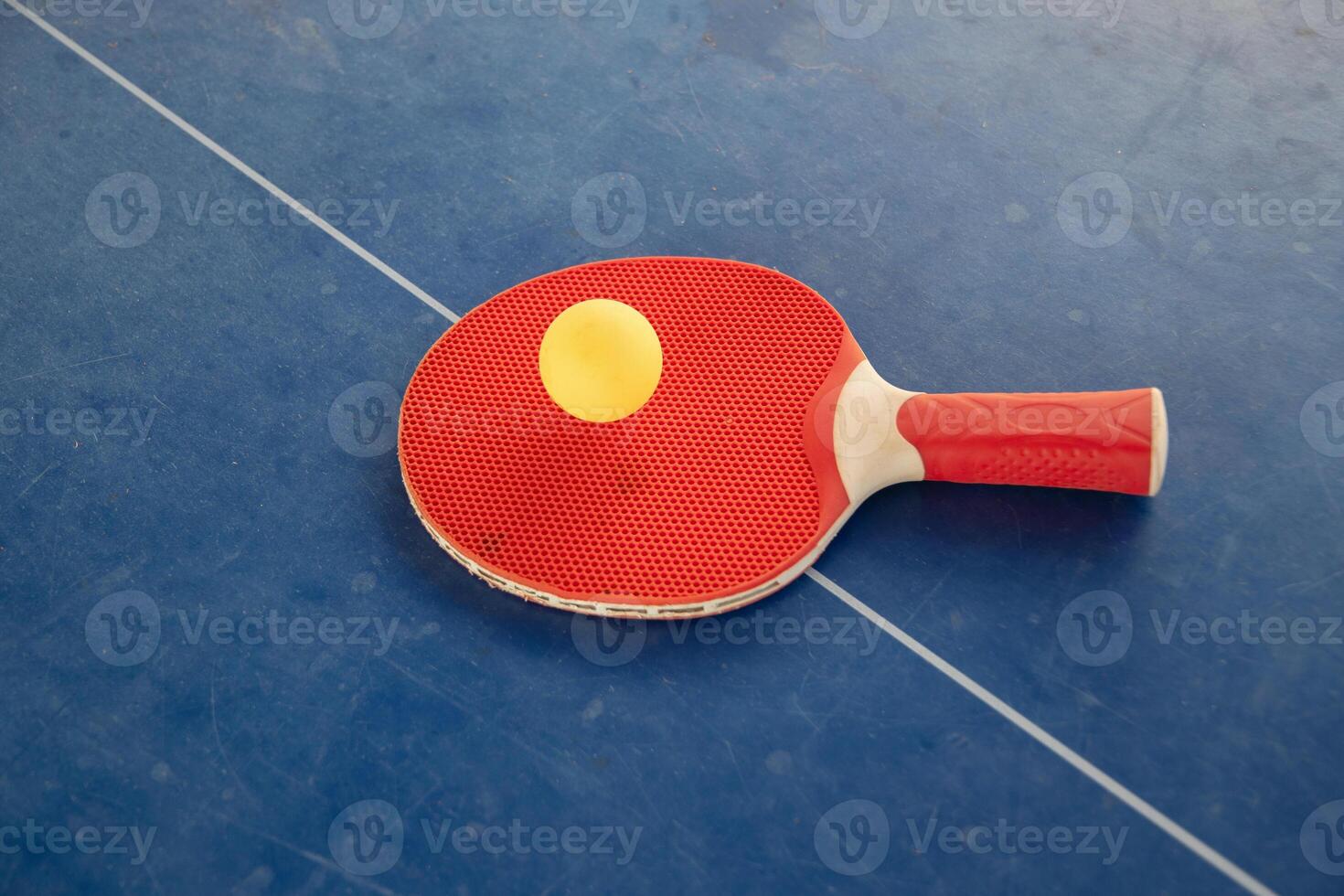 Red table tennis racket with a yellow ball between them on a blue background, ping pong sports equipment, symmetry concept regarding the center of the table with a white line, top view, photo