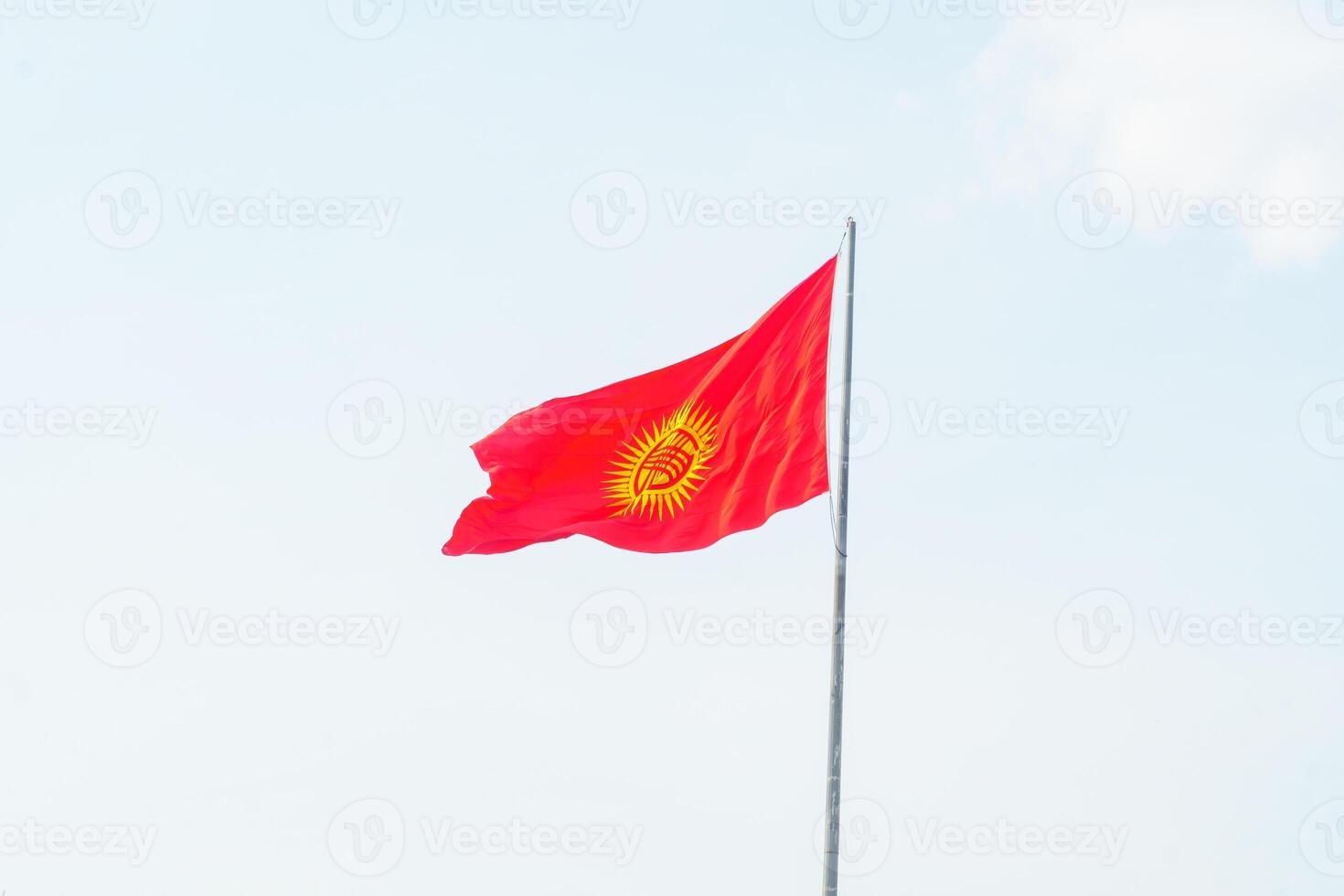 Kyrgyzstan national flag featuring a red background with a yellow sun and a traditional tunduk symbol. Symbol of unity and heritage. Waving prominently on a flagpole against a clear, blue sky. photo