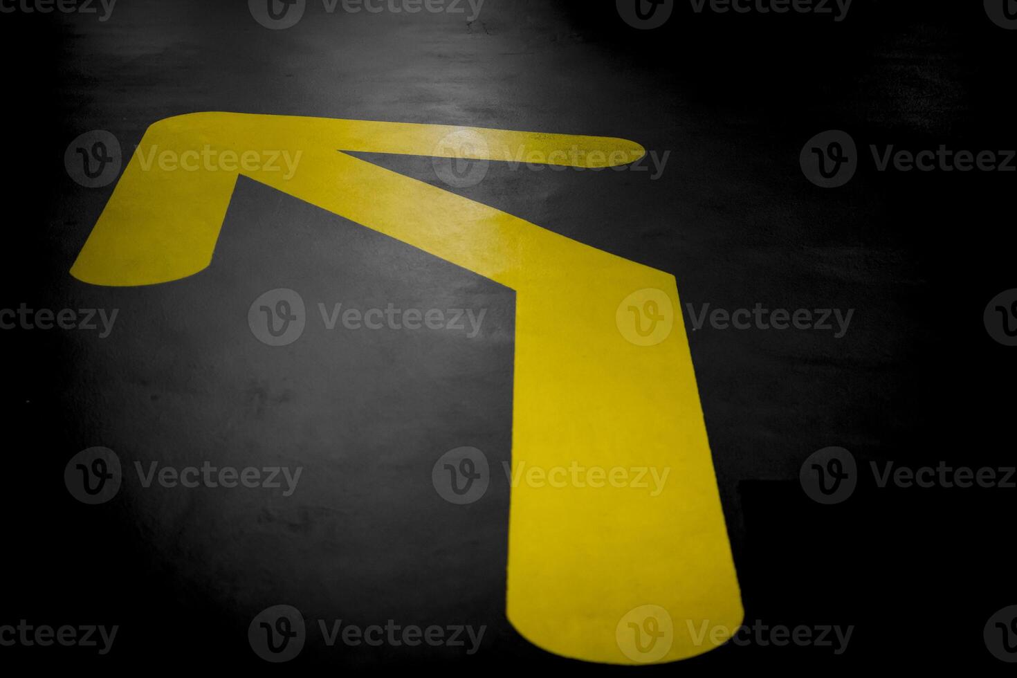 Yellow arrow on a dark asphalt surface, pointing towards the upper left corner, indicating directions photo